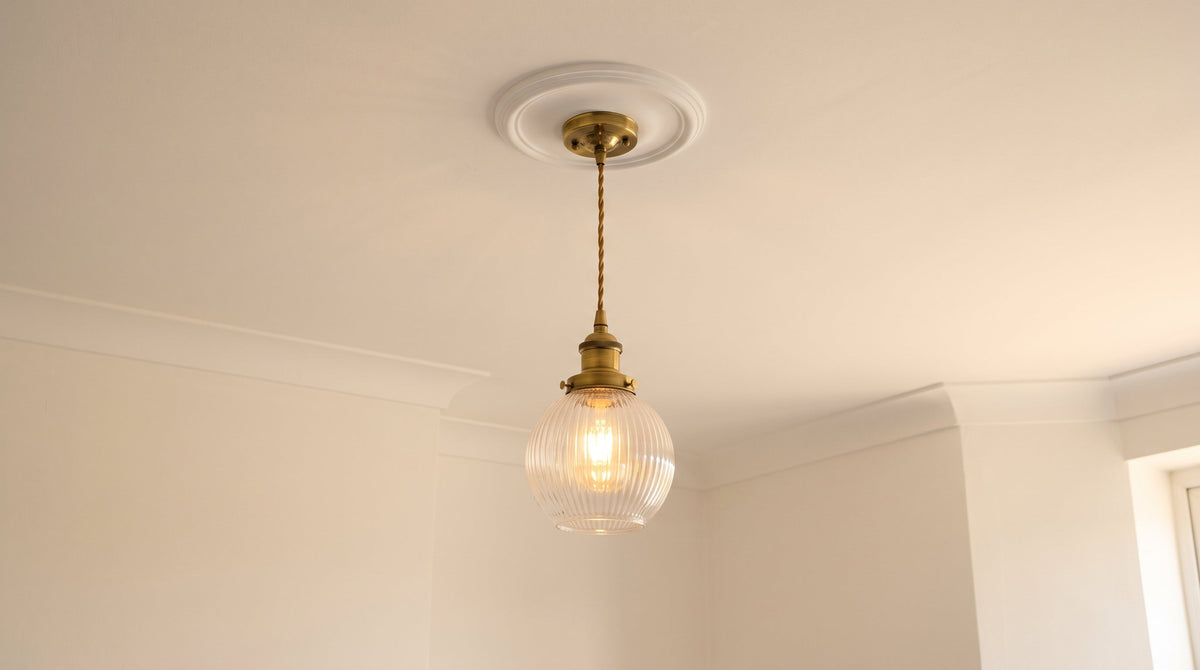 Rosace en laiton d'une suspension fixée au plafond, câble torsadé descendant vers la douille, sur un plafond clair à moulure ronde.