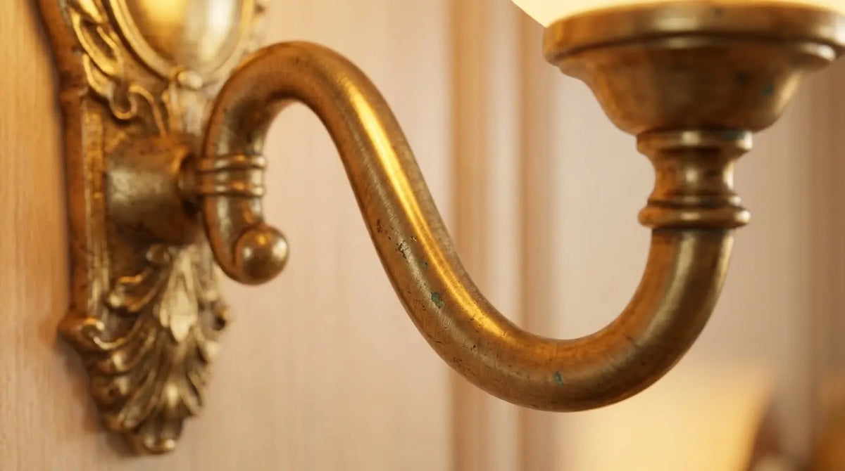 Gros plan en lumière rasante sur le bras doré d'une applique murale, le grain brossé du métal révélé par un reflet chaud allongé. Image