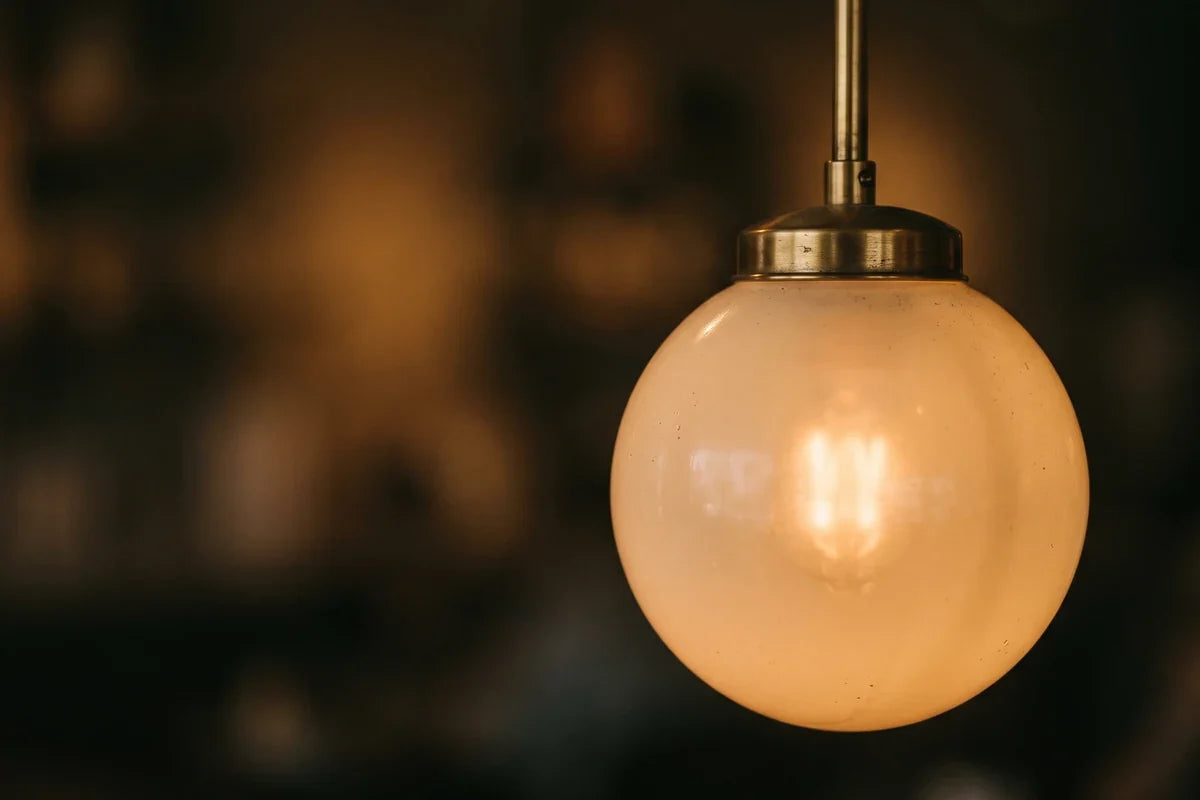 Choisir une ampoule : plan rapproché d'un globe de verre opalin allumé, la source diffusée en lumière chaude. Image