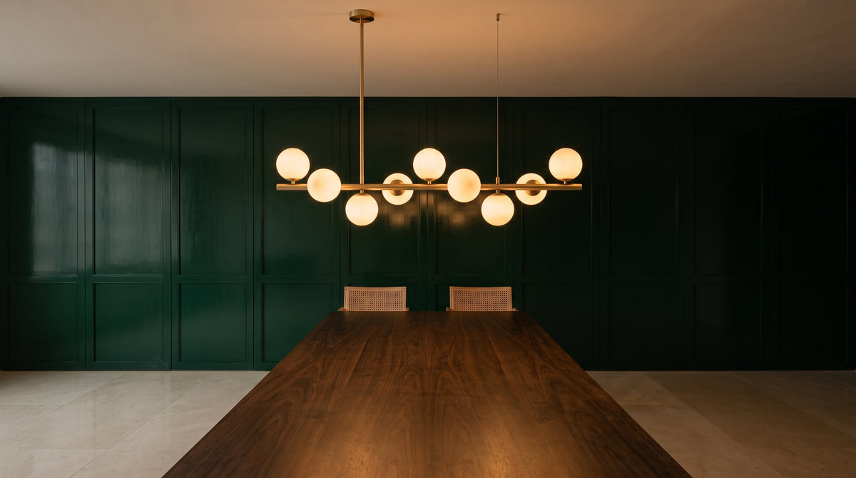Suspension linéaire à globes de verre opalin allumée au-dessus d'une table de salle à manger, mur en boiserie laquée vert profond.