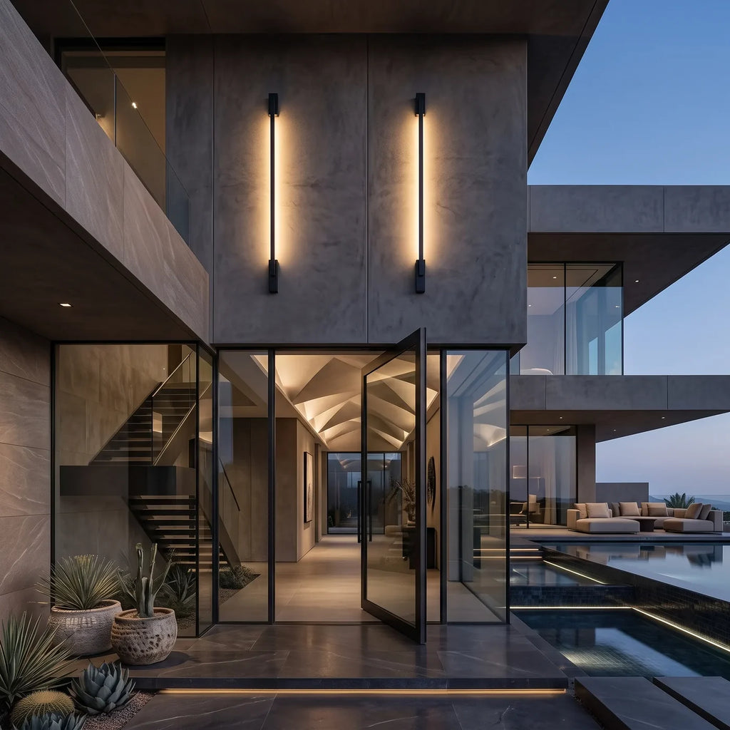 Deux tubes lumineux verticaux sur la façade en béton d'une villa, de part et d'autre de l'entrée vitrée