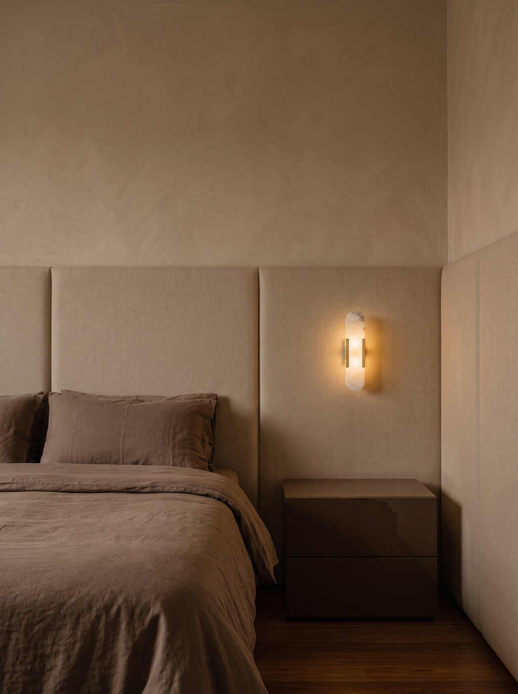 Applique Iéna en pierre claire et laiton au chevet d'un lit, sur un mur de limewash et panneaux de tissu