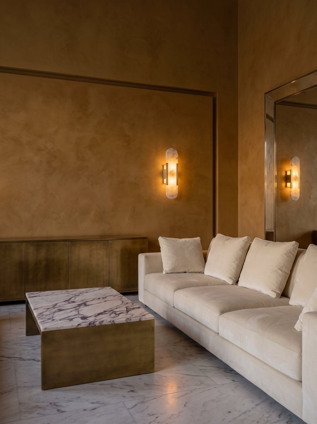 Deux appliques Iéna dans un salon au stuc ocre, canapé de velours ivoire et table basse Calacatta Viola