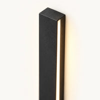 Extrémité d'une barre en fer noir texturé, fente lumineuse LED et halo chaud sur le mur