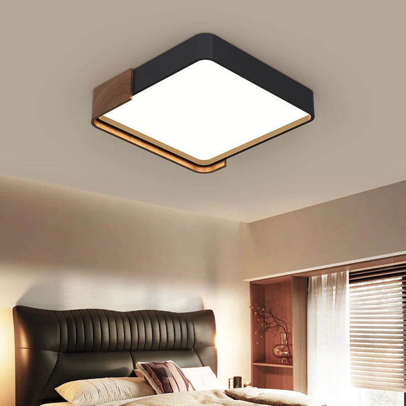 Plafonnier LED carré noir et bois allumé au plafond d'une chambre, au-dessus d'un lit à tête de cuir.
