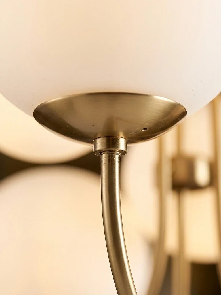 Gros plan sur la jonction d'un bras doré poli, de sa douille et d'un globe de verre opalin blanc