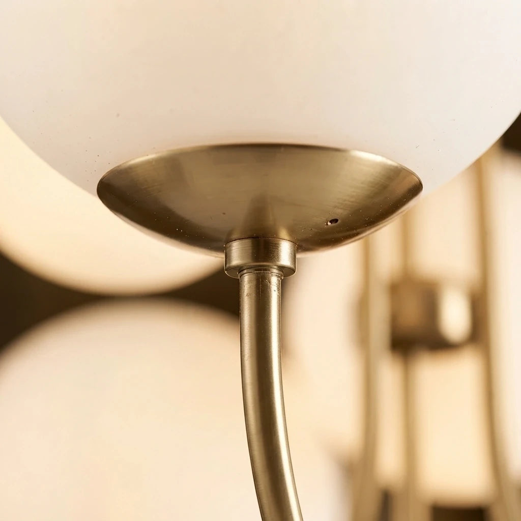 Gros plan sur la jonction d'un bras doré, de sa coupelle et d'un globe de verre opalin blanc