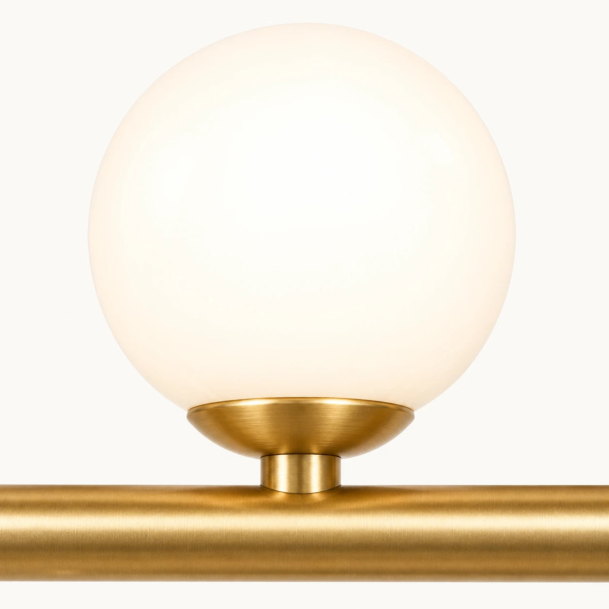 Détail d'un globe de verre opalin allumé et de sa bague doré satiné sur la barre de la suspension