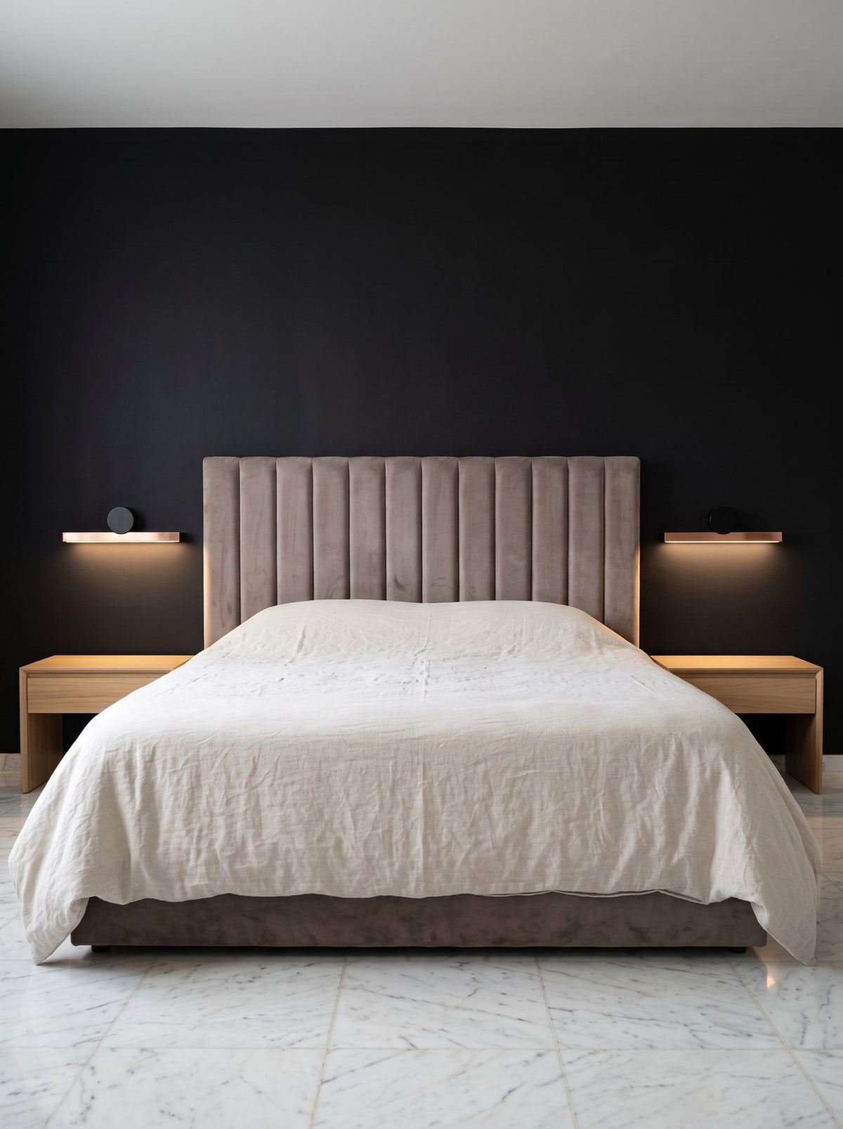 Barre lumineuse cuivrée au-dessus d'une tête de lit, mur noir mat et sol de marbre blanc